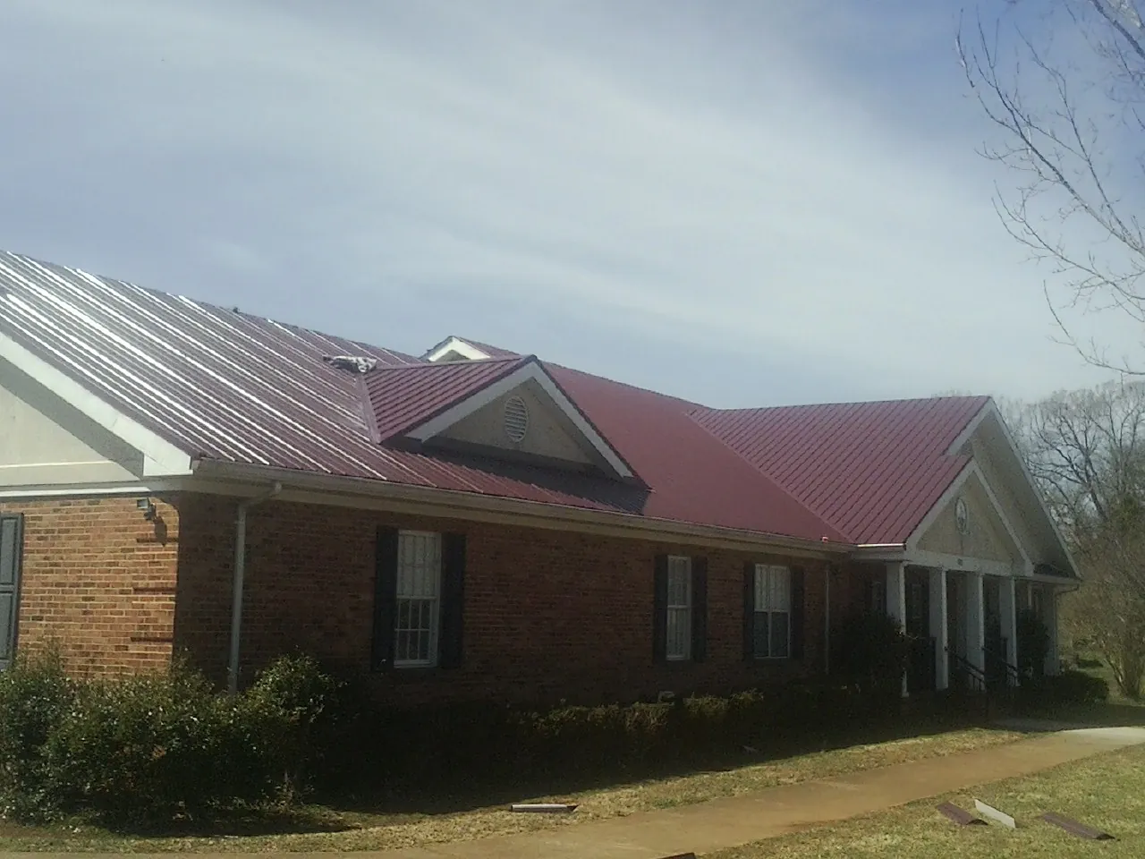 Red metal roof with gabled entries on a long brick building, from a Hail Damage Roof Repair job in Chambersburg