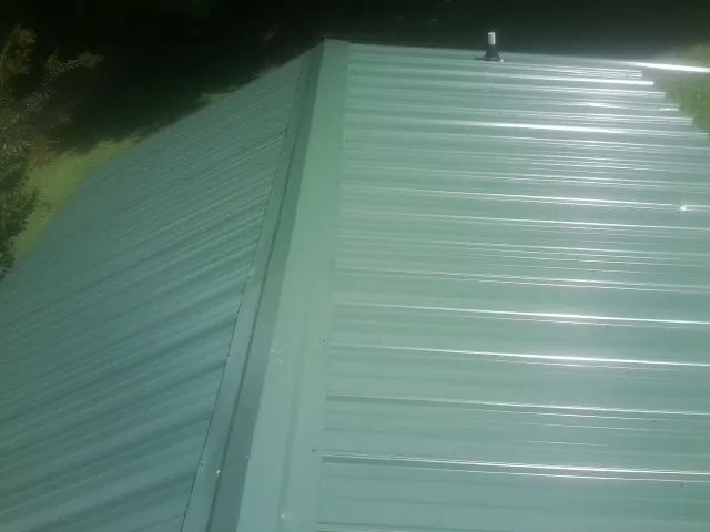 New green metal panels meeting at the ridge of a roof — Flat Roof Repair work by our crew in Chambersburg