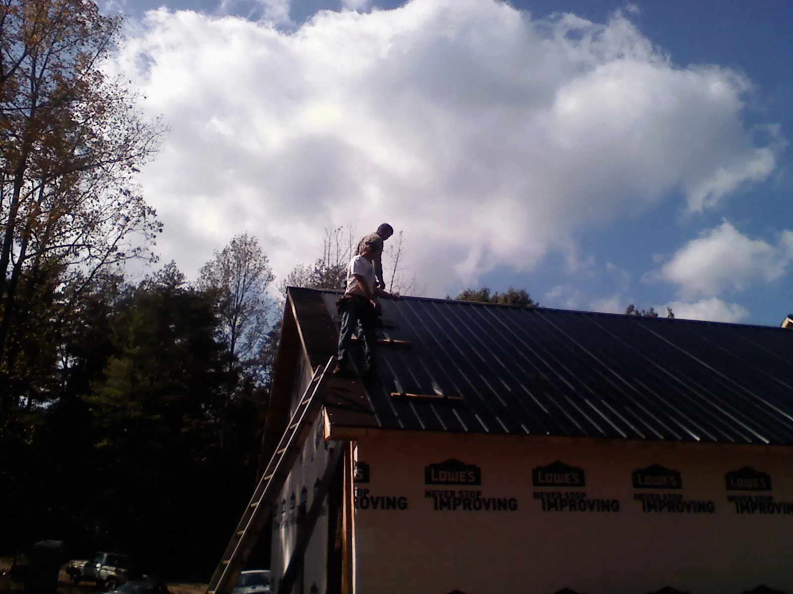 Roofer fastening dark metal panels high against a cloudy sky, from a Roof Inspection job in Chambersburg