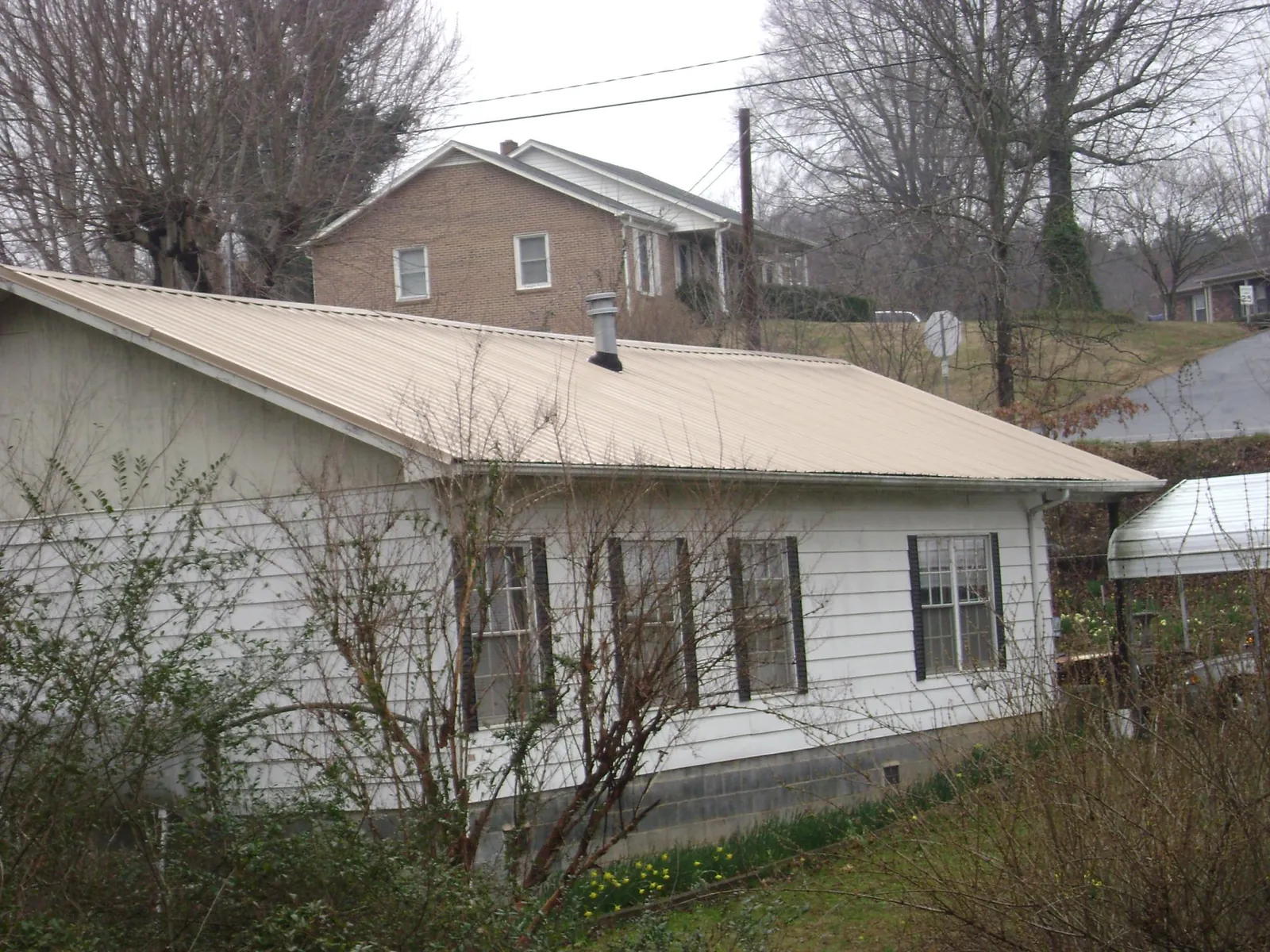 Tan metal roof on a white sided house set into a hillside — Commercial Roofing by Roofing Brothers in Chambersburg